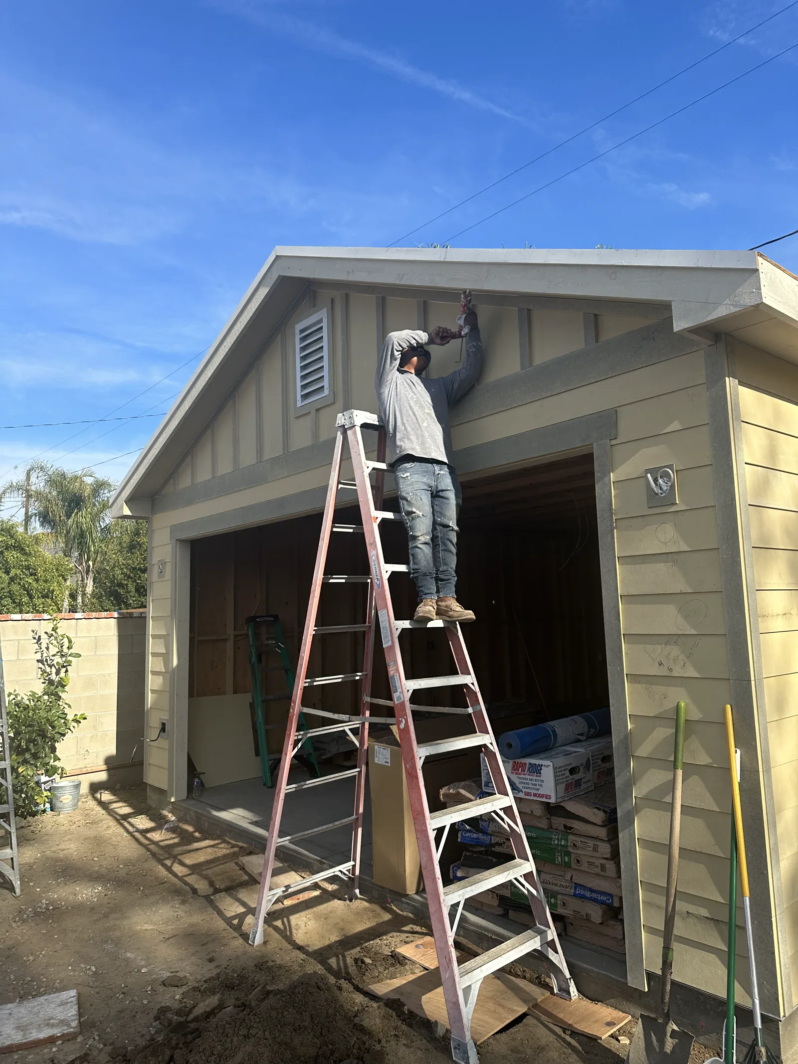 Crew member on a ladder finishing new board-and-batten and lap siding on an Arcadia garage