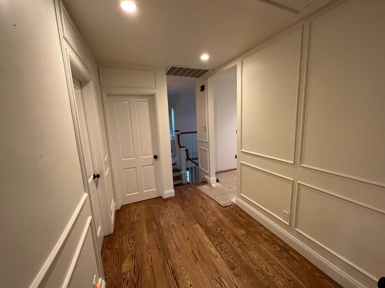 Upstairs hallway repainted in soft white with panel moulding walls, painted doors and oak floors