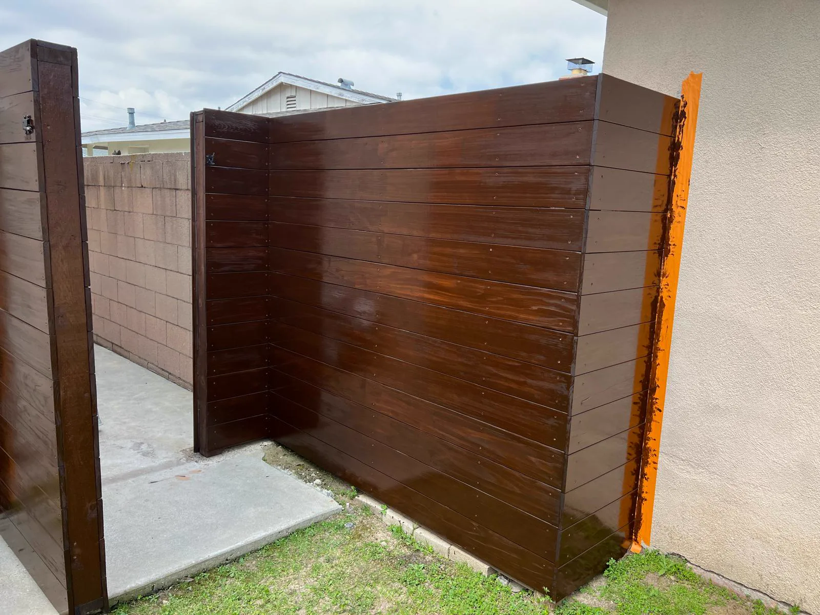 The same wood fence after cleaning and restaining in a rich dark brown