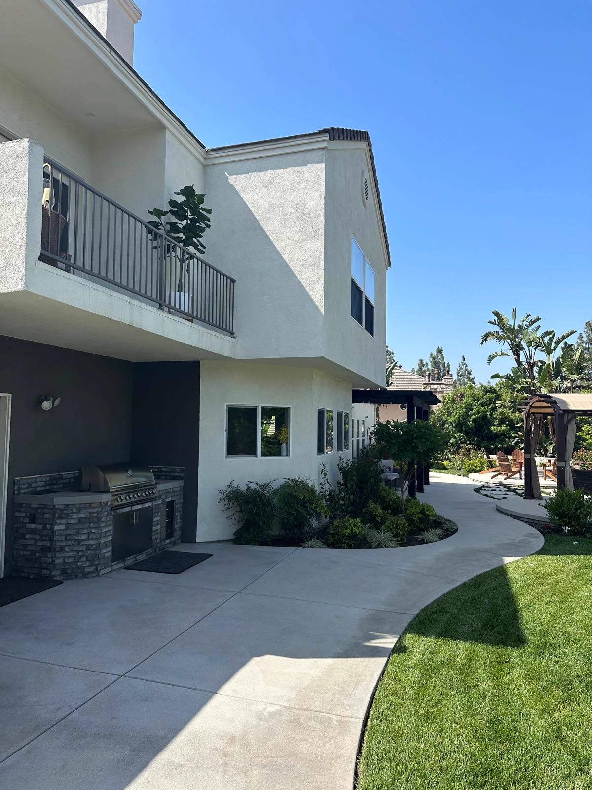 White stucco two-story Pasadena home with a balcony over the outdoor kitchen after exterior painting