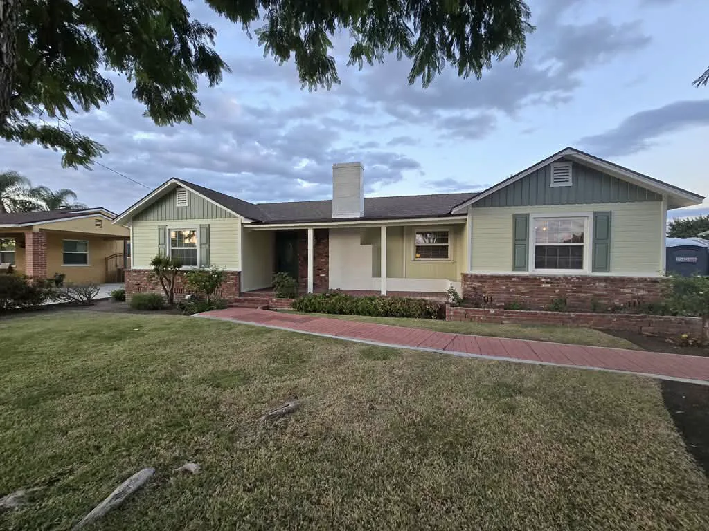 Pasadena ranch home repainted with a soft green body, sage board-and-batten gables and shutters, and white trim over a brick base