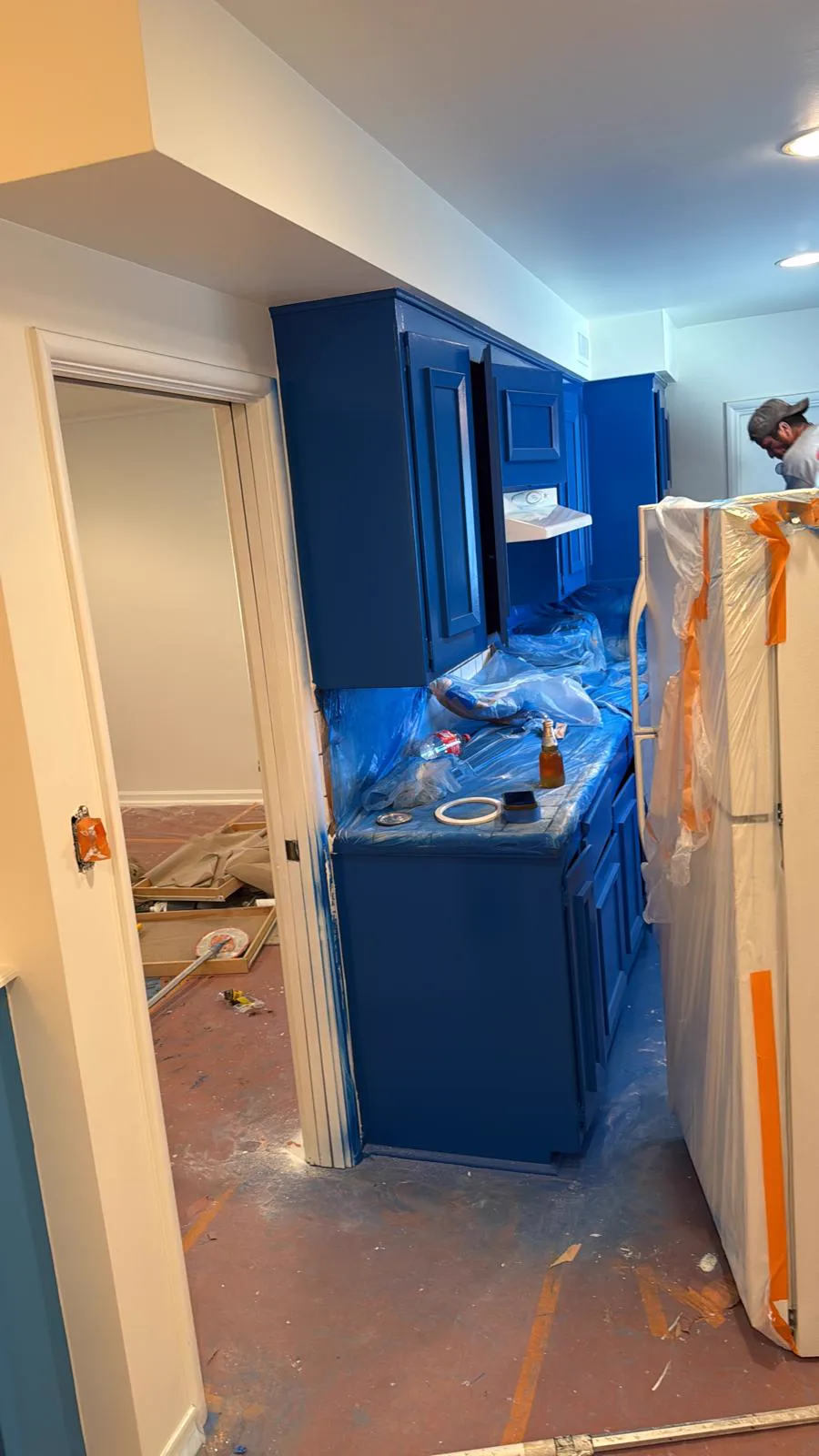 Kitchen cabinetry masked with plastic sheeting during painting in a San Gabriel home