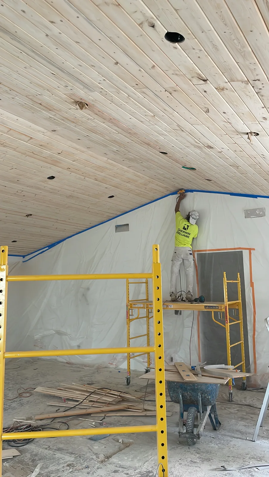 Painter on scaffolding masking a San Gabriel room in plastic below a tongue and groove wood ceiling